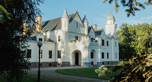 Valkoinen linna kukkulalla kesäisessä puistossa.