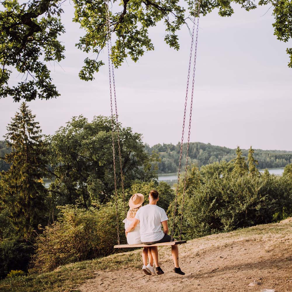Pariskunta istuu keinussa katsellen järvimaisemaa.