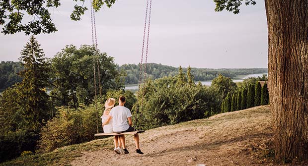 Pariskunta istuu keinussa katsellen järvimaisemaa.