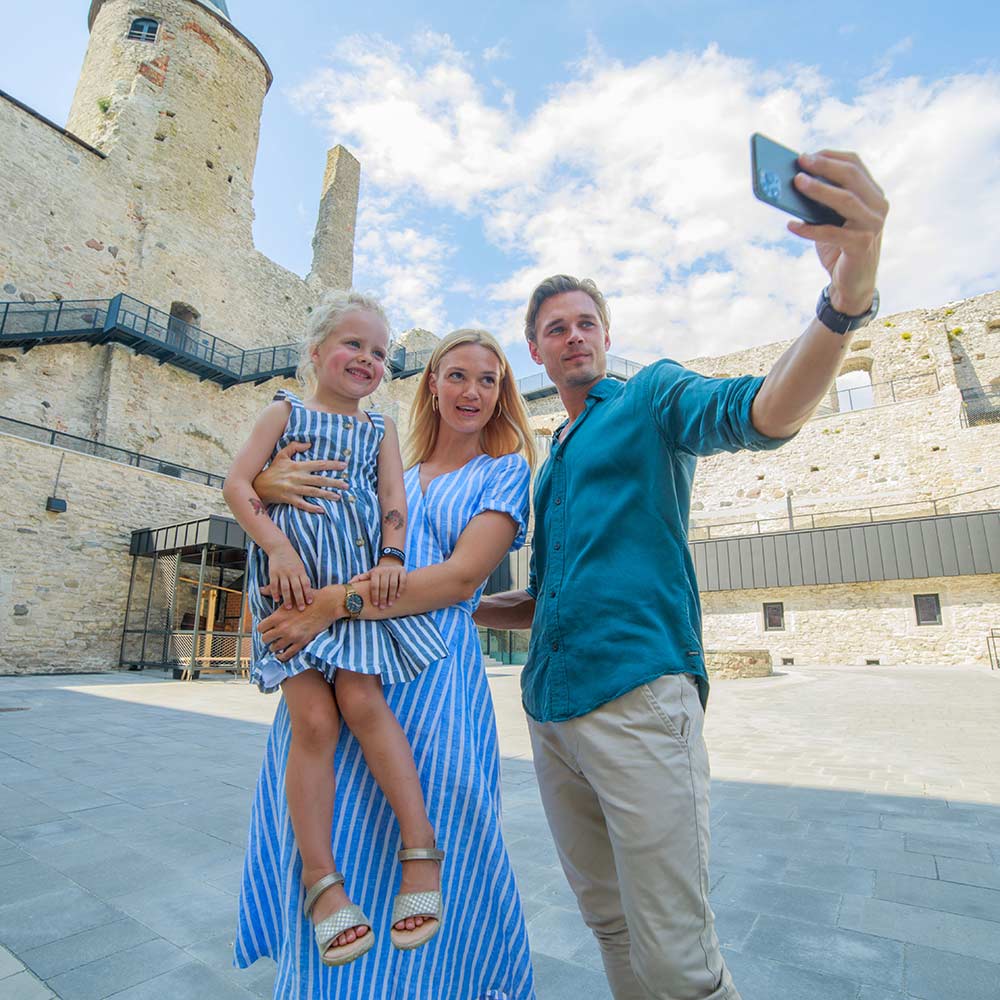 Perhe, jossa isä ottaa selfie-kuvaa. Perhe seisoo kivilinnan sisäpihalla.