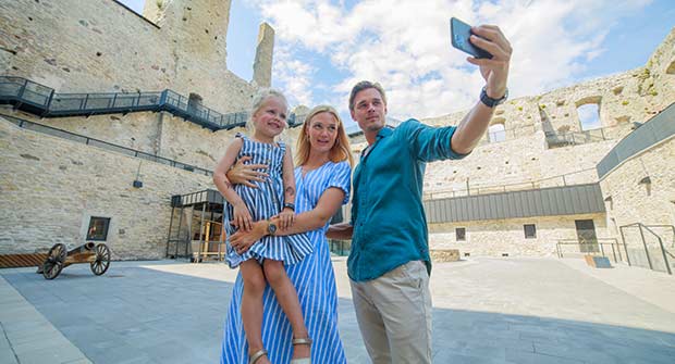 Perhe, jossa isä ottaa selfie-kuvaa. Perhe seisoo kivilinnan sisäpihalla.