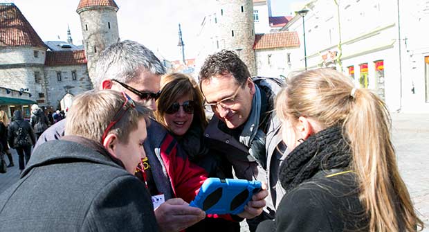 Ryhmä miehiä ja naisia katsoo iPadin näyttöä Tallinnan vanhassa kaupungissa.