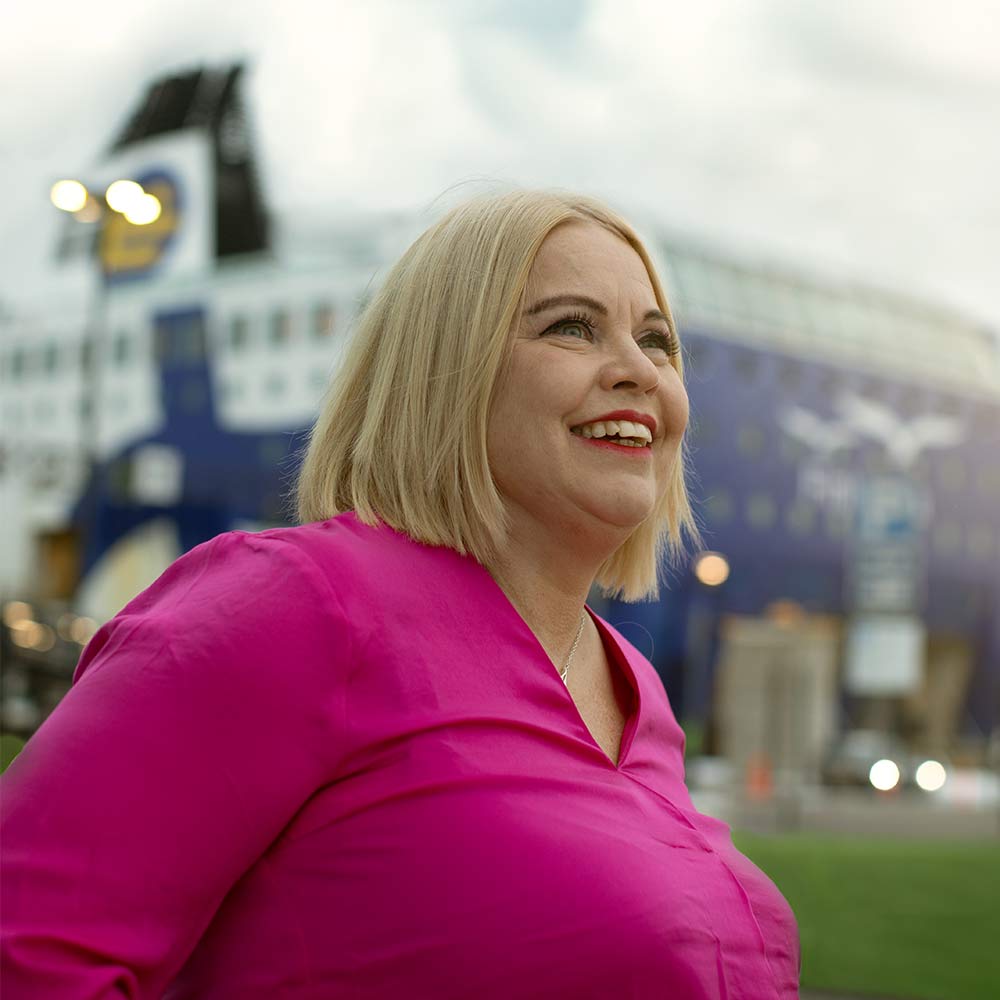Nainen hymyilee satamassa m/s Finlandia -aluksen näkyessä taustalla.