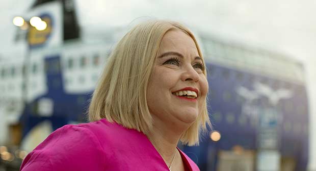 Nainen hymyilee satamassa m/s Finlandia -aluksen näkyessä taustalla.