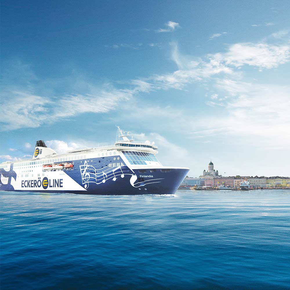 Sinivalkoinen m/s Finlandia -laiva merellä. Takana näkyy Helsinkiä, kuten esimerkiksi Tuomiokirkko.
