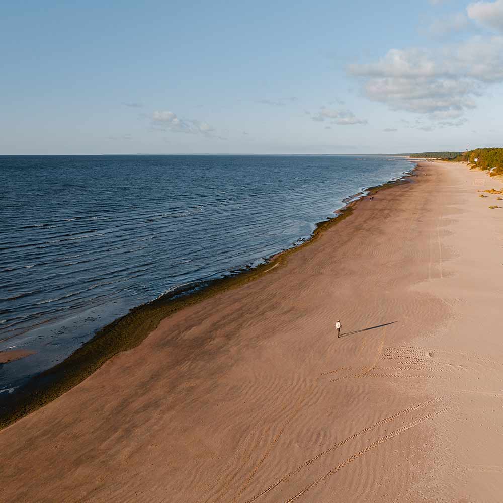 Pitkä hiekkaranta ja sininen meri kesällä. Ihminen kävelee rannalla.