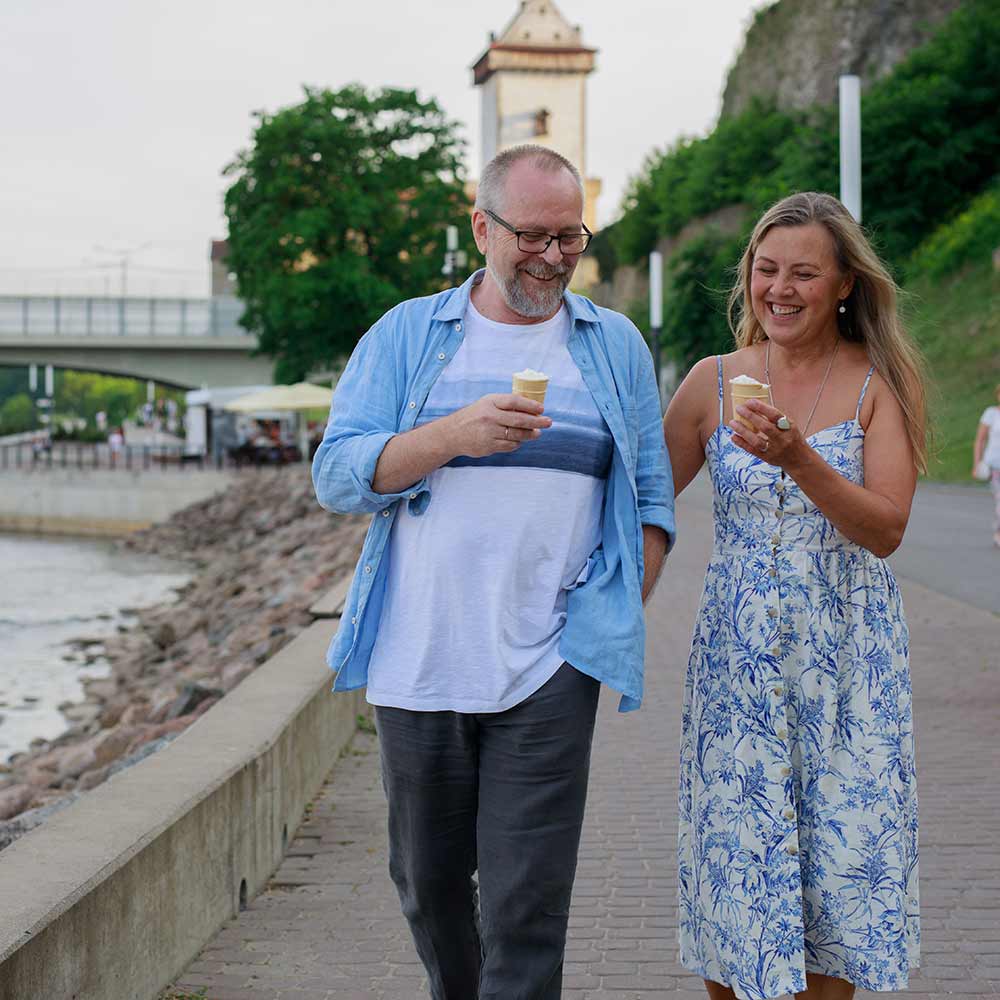 Mies ja nainen kävelevät jäätelöt kädessä joen viertä kesäisenä iltana.