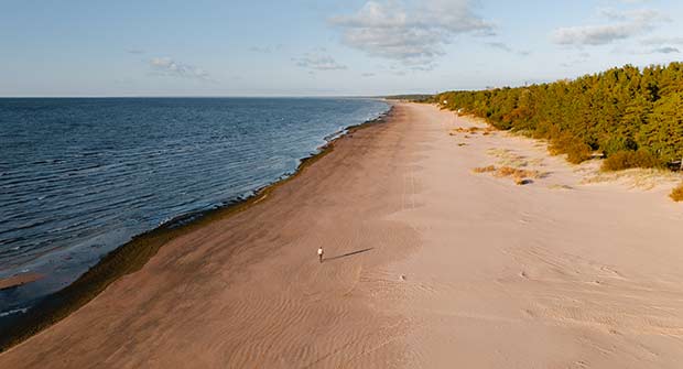 Pitkä hiekkaranta ja sininen meri kesällä. Ihminen kävelee rannalla.