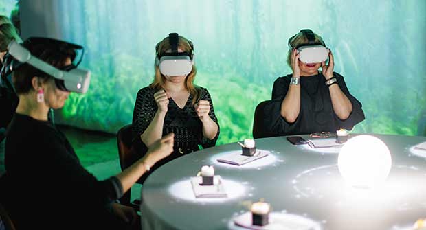 Kaksi naista istuu ruokapöydässä virtuaalitodellisuuslasit päässä.