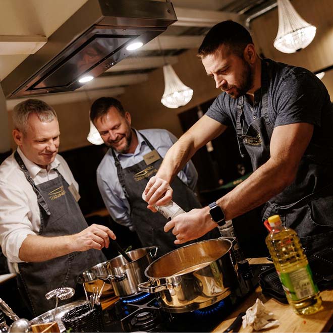 Kolme miestä laittamassa ruokaa.