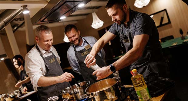 Kolme miestä laittamassa ruokaa.